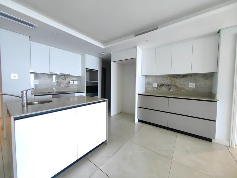 Modern kitchen featuring sleek handleless cabinetry, stone countertops, integrated appliances, and a central island with an undermount sink.