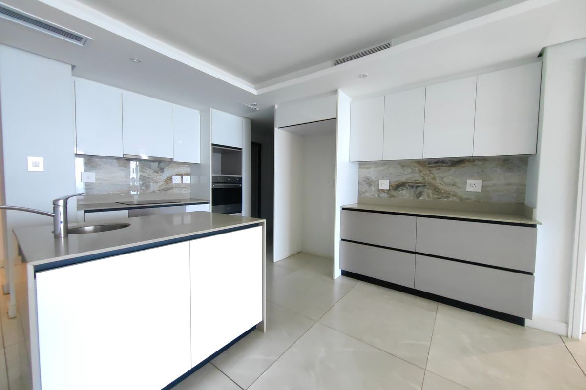 Modern kitchen featuring sleek handleless cabinetry, stone countertops, integrated appliances, and a central island with an undermount sink.