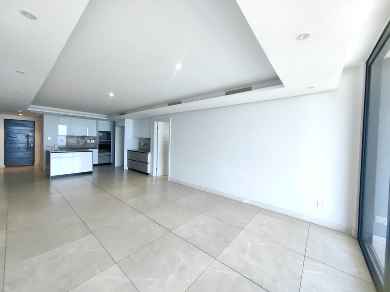 A spacious, modern open-plan living and kitchen area featuring large format floor tiles, recessed ceiling lighting, and sleek built-in cabinetry.
