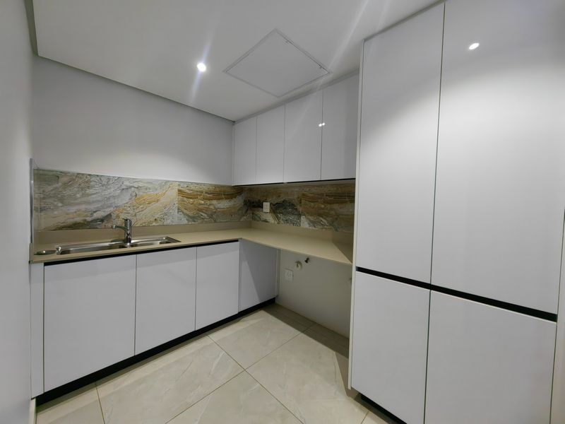 A modern, clean scullery featuring white handleless cabinetry, stone countertops, a stainless steel sink, and decorative stone splashbacks.