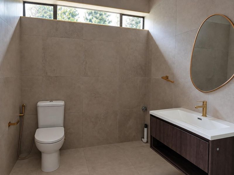 Modern bathroom featuring large-format neutral wall tiles, a floating vanity with integrated basin, brass fixtures, and a high-level window for natural light.
