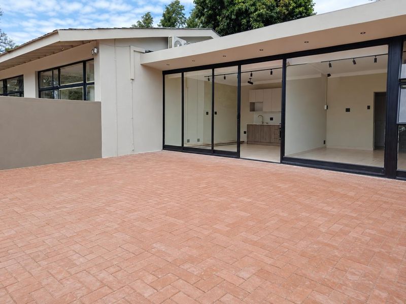 A spacious rear paved patio area featuring large sliding glass doors that provide seamless access to the open-plan interior living space.