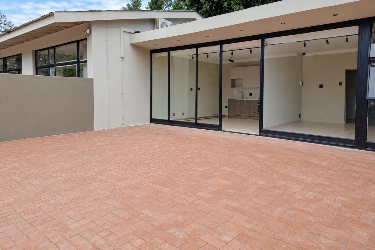 A spacious rear paved patio area featuring large sliding glass doors that provide seamless access to the open-plan interior living space.