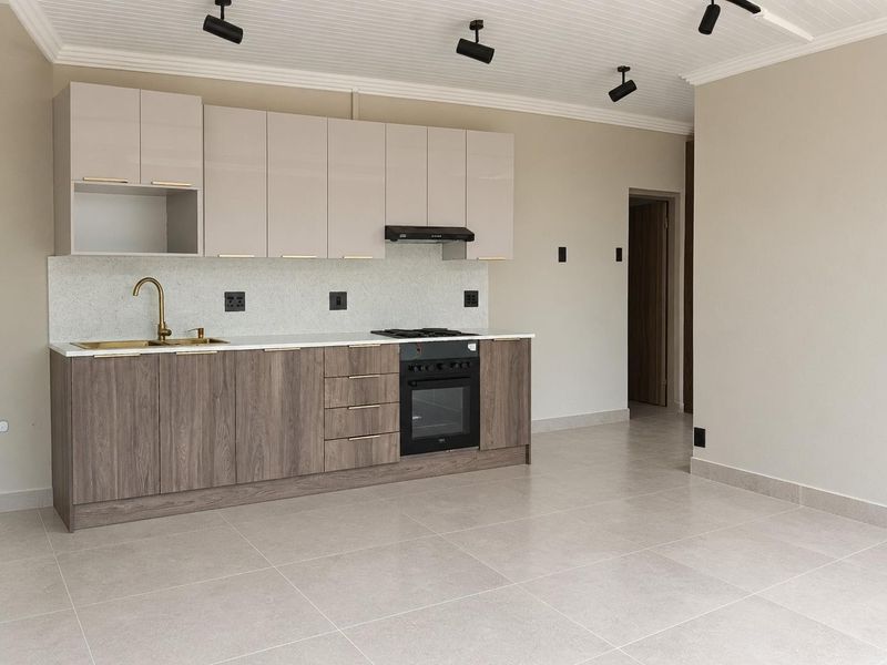 Modern open-plan kitchen featuring sleek wood-grain lower cabinets, neutral upper cabinetry, stone countertops, brass fixtures, and integrated appliances.