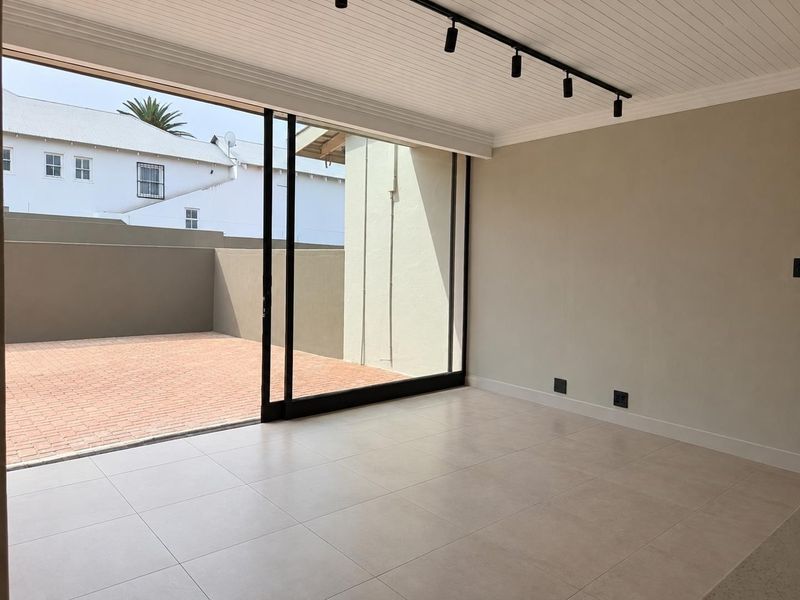 Bright and modern living area featuring large sliding glass doors that open onto a paved patio, complemented by sleek track lighting and neutral tiled floors.