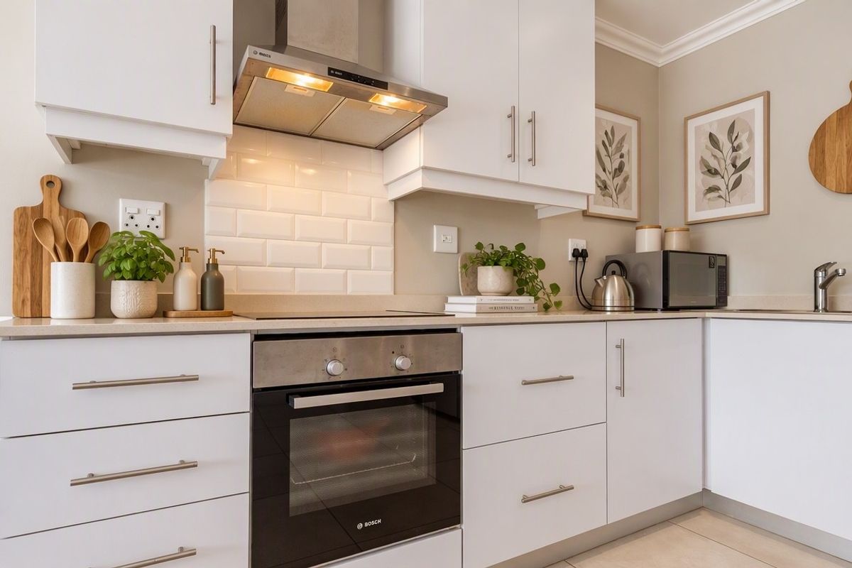 Modern kitchen featuring white cabinetry, subway tile backsplash, stainless steel built-in oven, extractor fan, and stone countertops.