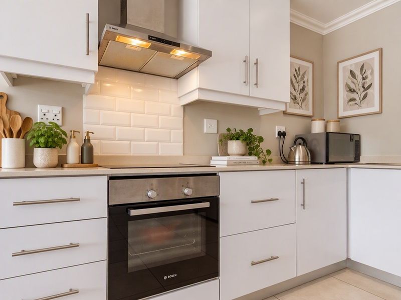 Modern kitchen featuring white cabinetry, subway tile backsplash, stainless steel built-in oven, extractor fan, and stone countertops.