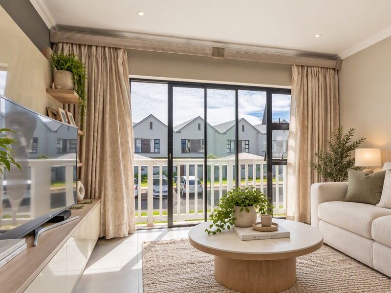 A bright and modern living room featuring large sliding glass doors that open onto a balcony, with neutral finishes and recessed lighting.