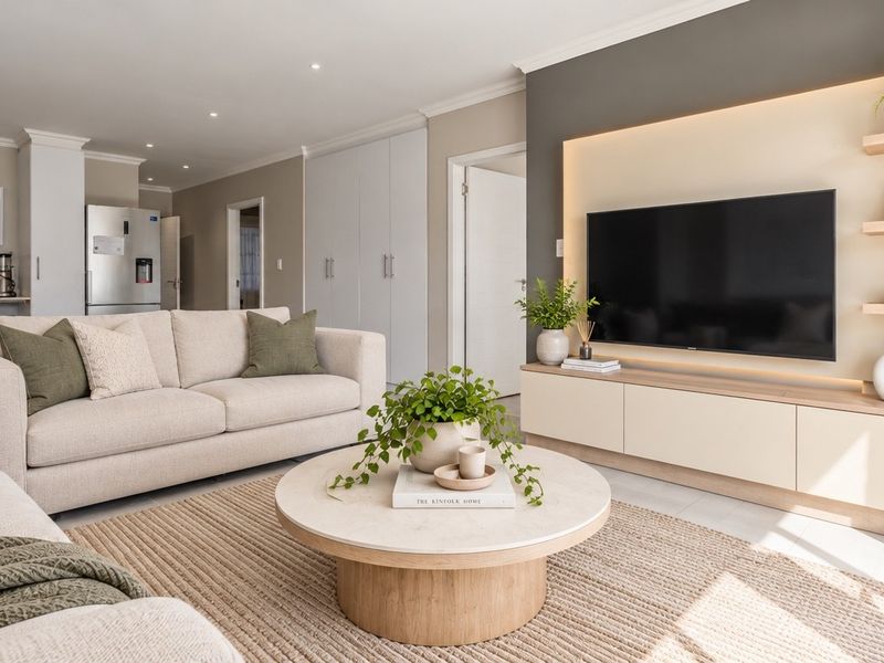 Modern open-plan living area featuring a custom built-in media unit with integrated lighting, neutral finishes, and seamless flow into the adjacent kitchen space.