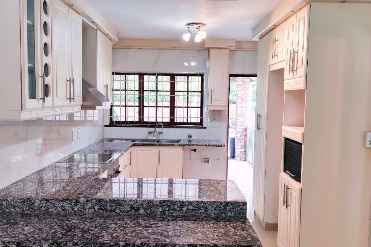 A well-maintained kitchen featuring granite countertops, ample built-in cabinetry, integrated appliances, and tiled flooring, offering a clean and functional workspace.