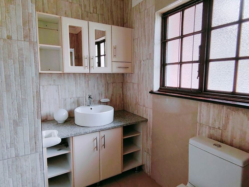 A clean bathroom featuring a modern vessel sink, vanity storage, wall-mounted mirror cabinet, and a standard toilet with tiled finishes throughout.
