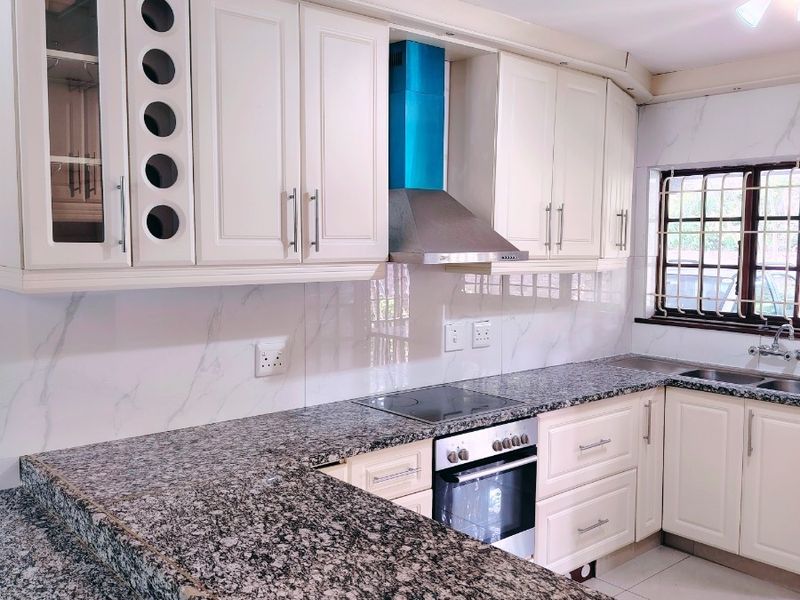 A well-maintained kitchen featuring granite countertops, built-in cabinetry, integrated oven and hob, and a tiled backsplash with a window overlooking the exterior.