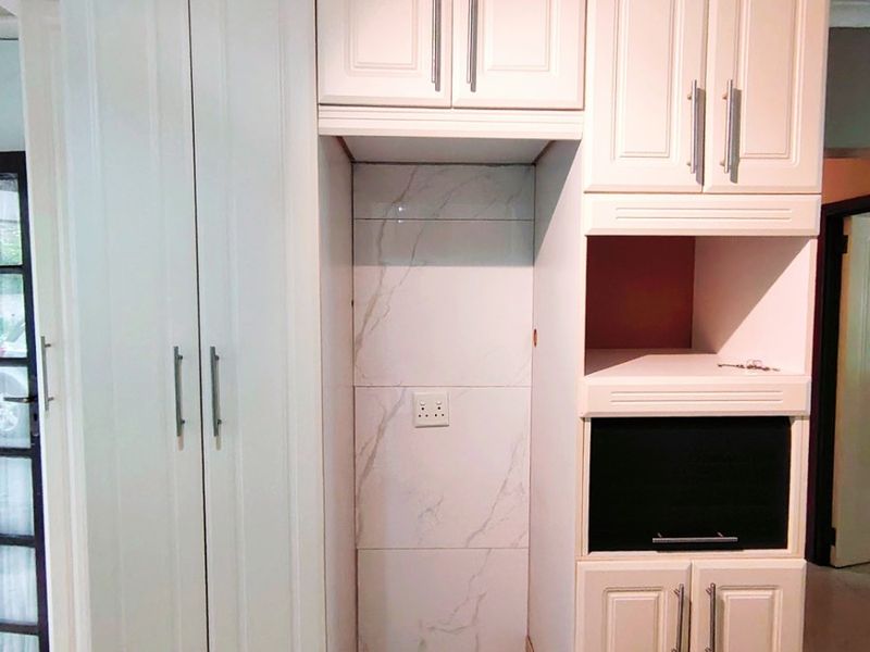 A clean, modern kitchen storage unit featuring white cabinetry, a dedicated fridge recess with marble-look tiling, and a built-in oven.