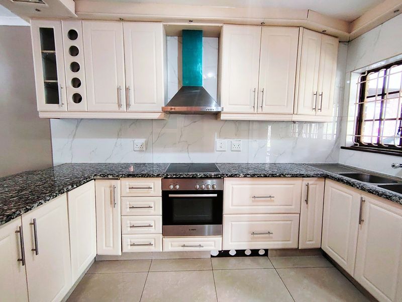 A well-maintained kitchen featuring cream cabinetry, granite countertops, a built-in oven with electric hob, and a modern marble-look splashback.