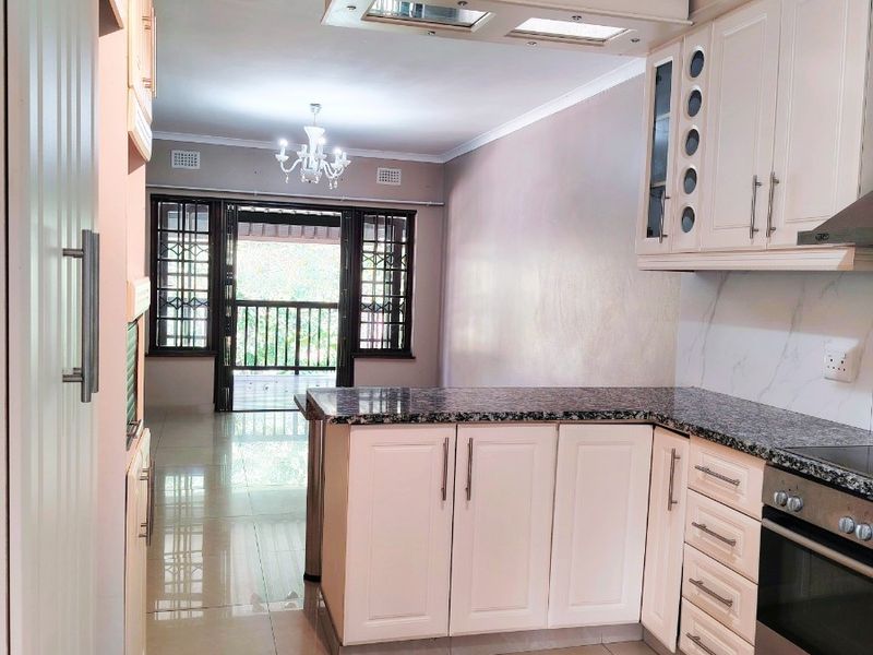 Open-plan kitchen featuring granite countertops, built-in oven, and hob, flowing into a living area with access to a balcony through a security gate.