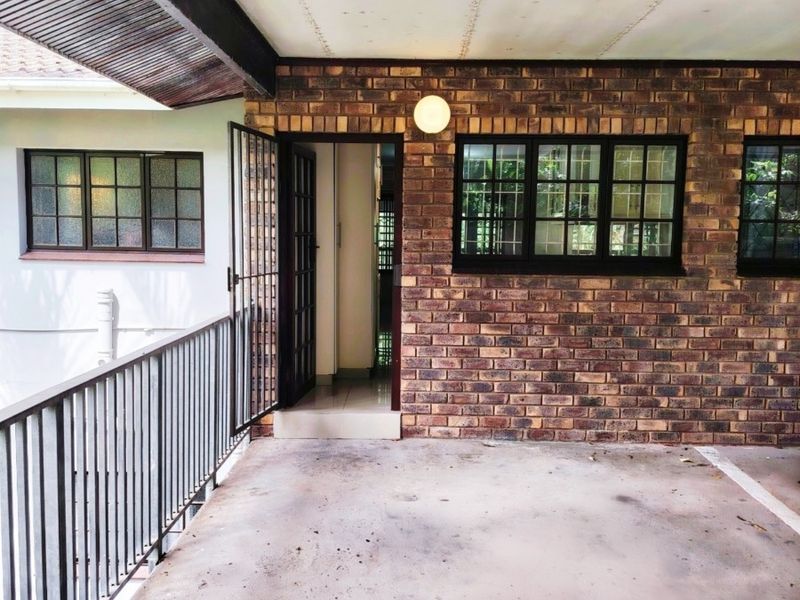 A covered balcony or patio area featuring exposed brick walls, a metal balustrade, and direct access to the apartment interior.