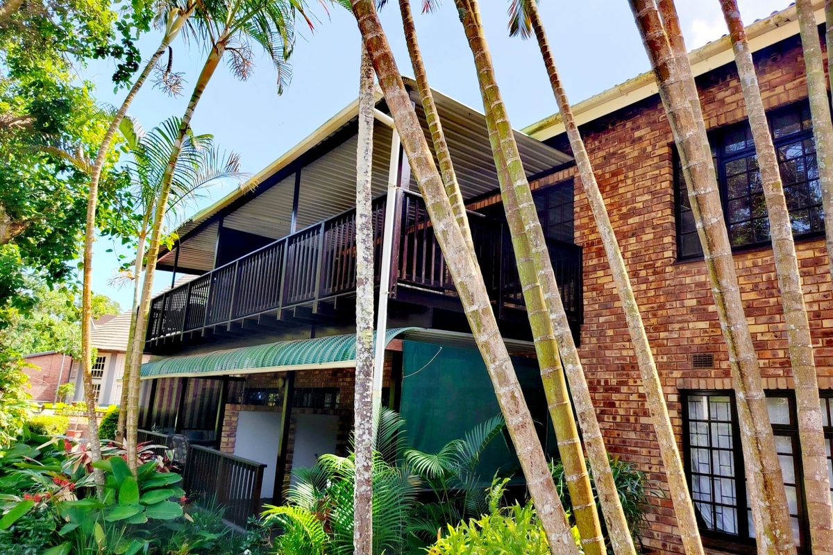 Rear view of a face brick apartment building featuring a covered balcony with timber railings and established garden surroundings.