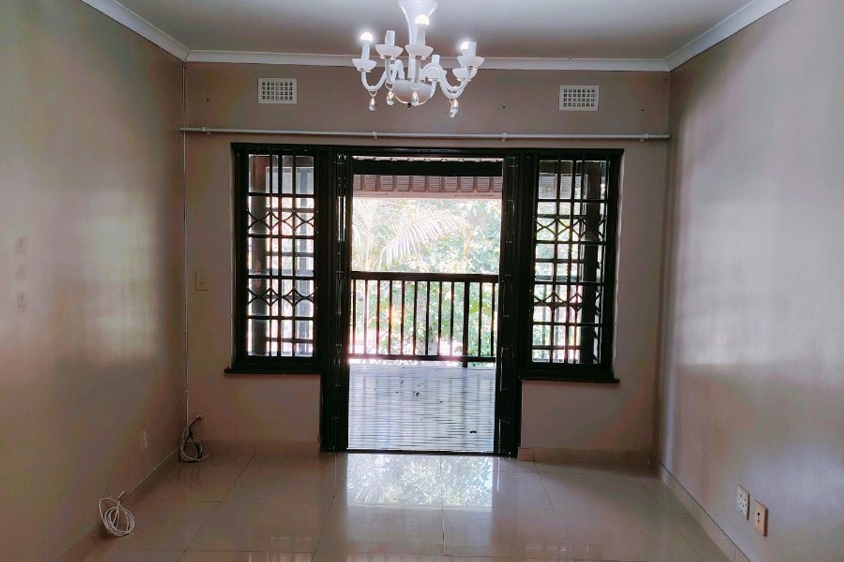 An empty living room featuring polished tile flooring, a central chandelier, and direct access to an outdoor balcony through a secure sliding door.