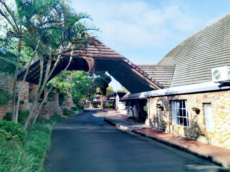 Exterior view of the apartment complex entrance featuring a distinctive stone-clad archway, tiled roofing, and a paved driveway approach.