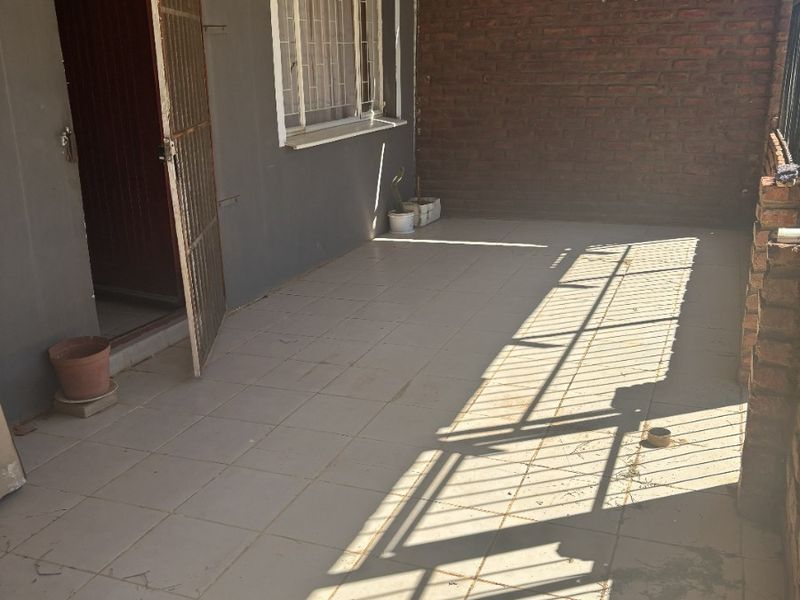 A covered outdoor patio area featuring tiled flooring, an exposed brick wall, and a wall-mounted air conditioning unit.