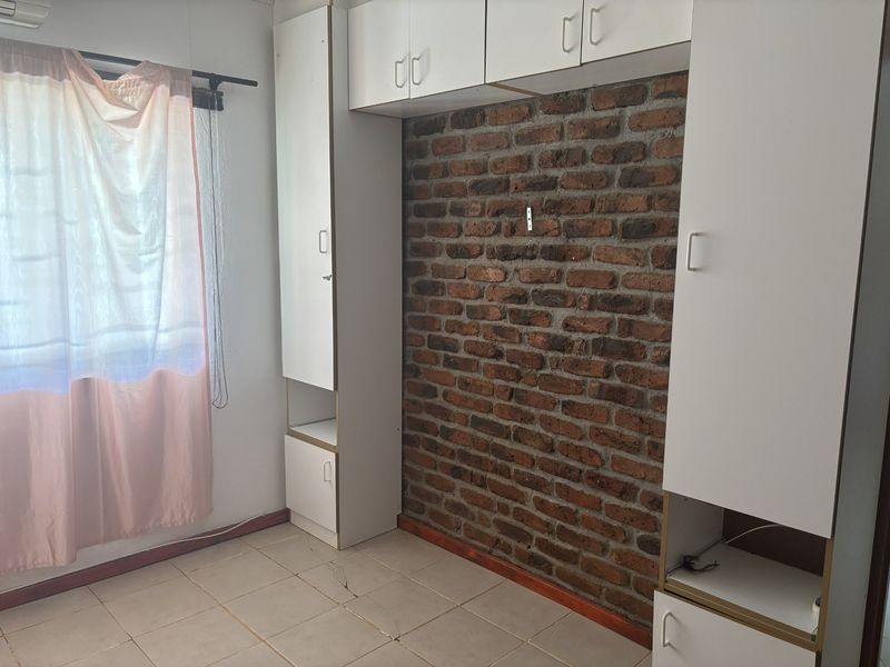 Bedroom featuring built-in white cabinetry, an exposed brick feature wall, tiled flooring, and an air conditioning unit.