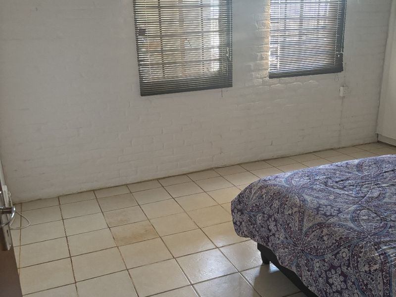 A bedroom featuring painted brick walls, tiled flooring, and an installed air conditioning unit, providing a functional space with potential for cosmetic updates.