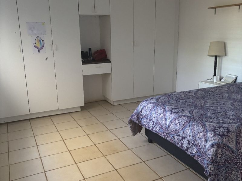 Spacious bedroom featuring extensive built-in cupboards and tiled flooring, offering a functional layout ready for cosmetic updates.