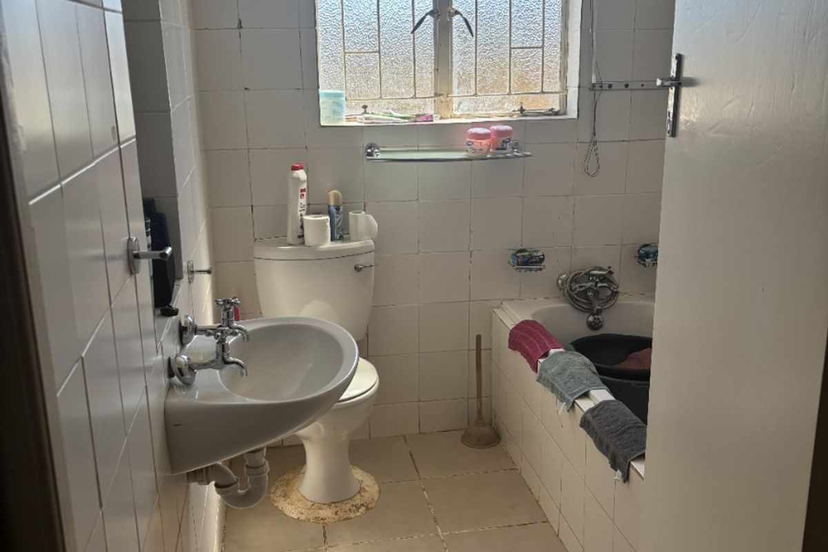 A compact bathroom featuring a wall-mounted basin, toilet, and built-in bathtub with tiled finishes, requiring cosmetic updates to improve its overall condition.