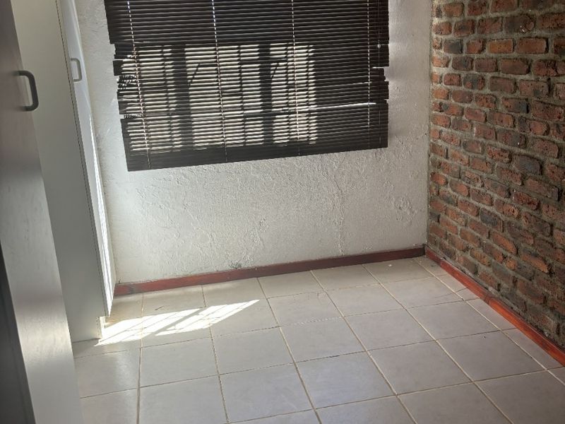An empty bedroom featuring tiled flooring, an exposed brick feature wall, and built-in cupboards with venetian blinds.
