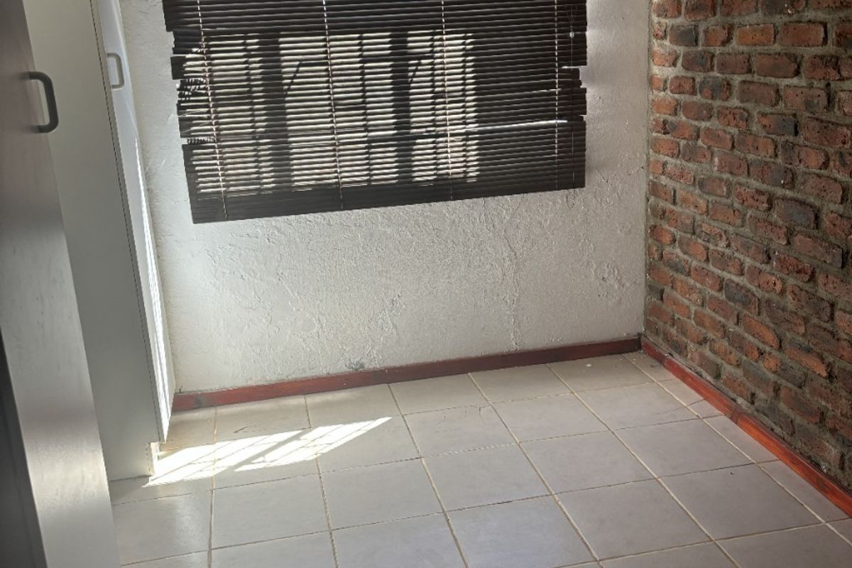 An empty bedroom featuring tiled flooring, an exposed brick feature wall, and built-in cupboards with venetian blinds.
