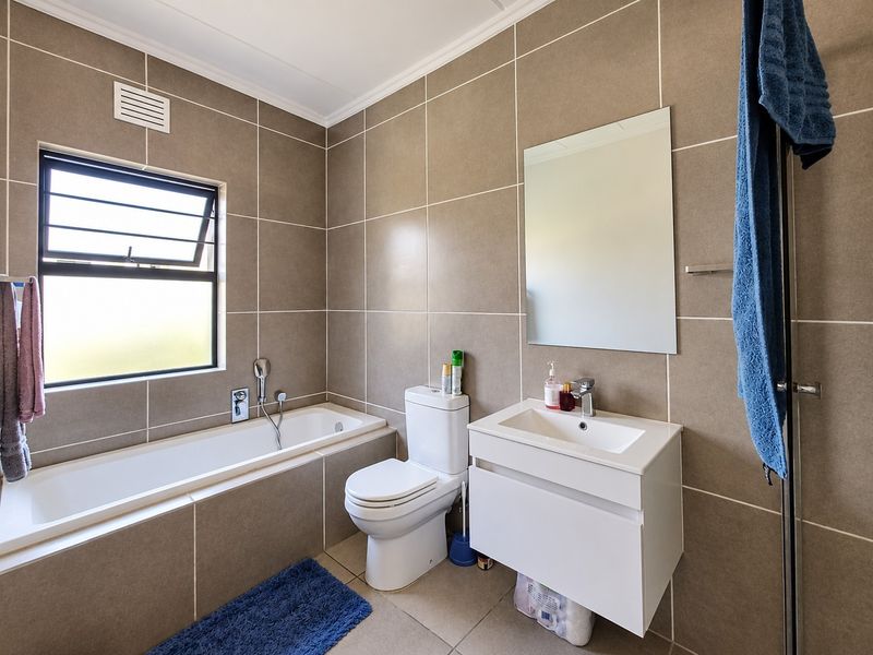 A modern, well-maintained bathroom featuring full-height wall tiling, a wall-mounted vanity, a built-in bathtub, and a louver window for ventilation.