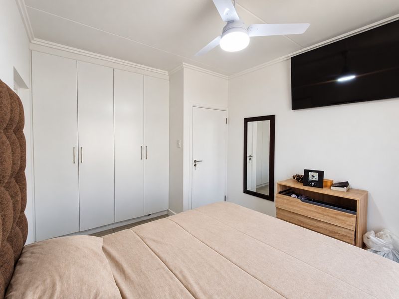 A well-maintained bedroom featuring built-in cupboards, a ceiling fan, and neutral finishes, providing a clean and functional living space.