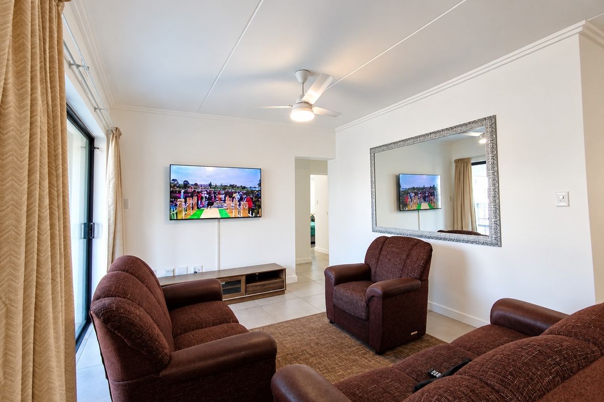 A well-maintained living room featuring tiled flooring, a ceiling fan, and a sliding glass door providing natural light.