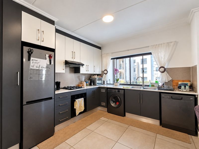 Modern kitchen featuring two-tone cabinetry, gas hob, built-in oven, integrated appliances, and tiled flooring with ample natural light.