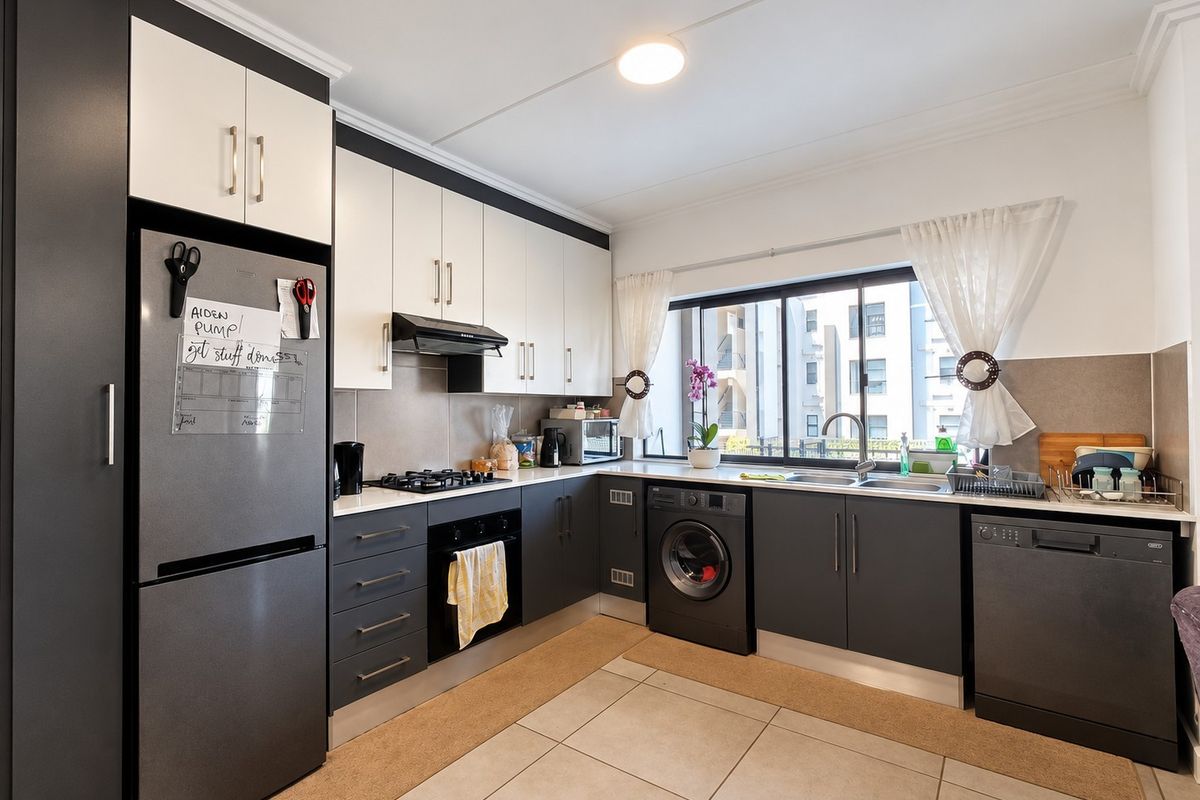 Modern kitchen featuring two-tone cabinetry, gas hob, built-in oven, integrated appliances, and tiled flooring with ample natural light.