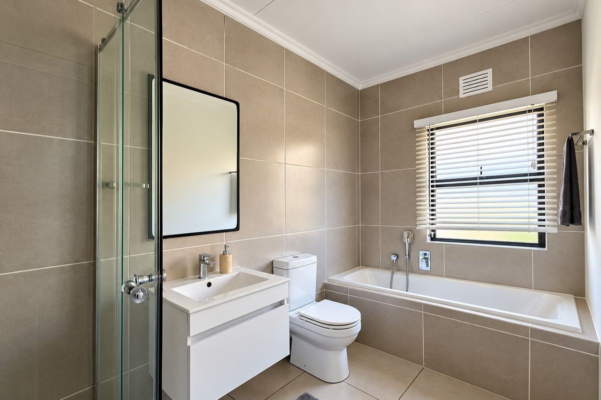 Modern bathroom featuring a wall-mounted vanity, built-in bathtub, separate shower enclosure, and neutral floor-to-ceiling tiling.