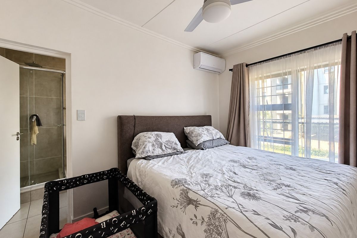 A well-maintained bedroom featuring a ceiling fan, split-system air conditioning, and an attached en-suite bathroom with a shower.