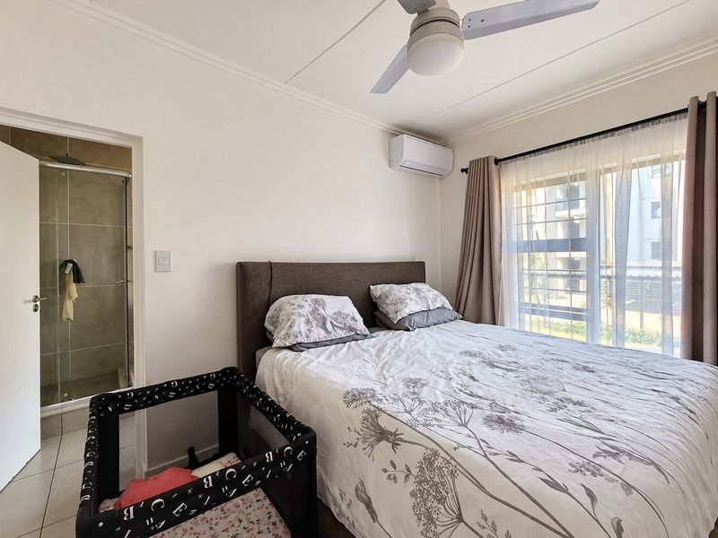 A well-maintained bedroom featuring a ceiling fan, split-system air conditioning, and an attached en-suite bathroom with a shower.