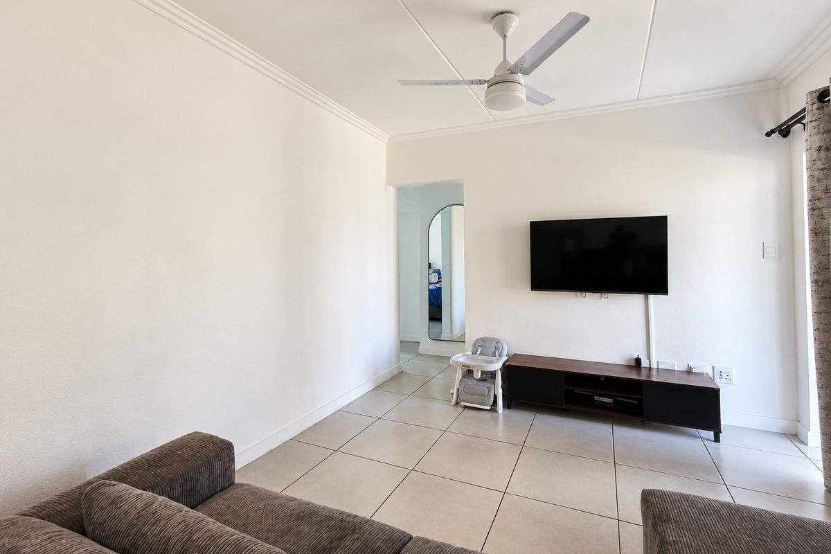 A bright living room featuring neutral tiled flooring, a ceiling fan, and coved ceiling details, providing a clean and functional space.