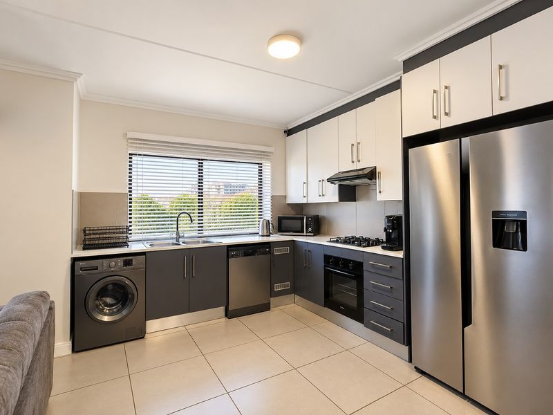 Modern kitchen featuring two-tone cabinetry, stainless steel appliances, integrated dishwasher, gas hob, and tiled flooring with ample natural light.