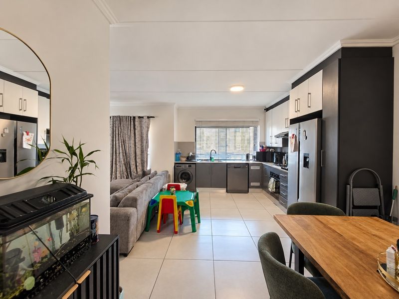 A modern open-plan living and kitchen area featuring sleek cabinetry, integrated appliances, tiled flooring, and a functional layout connecting the kitchen to the living space.