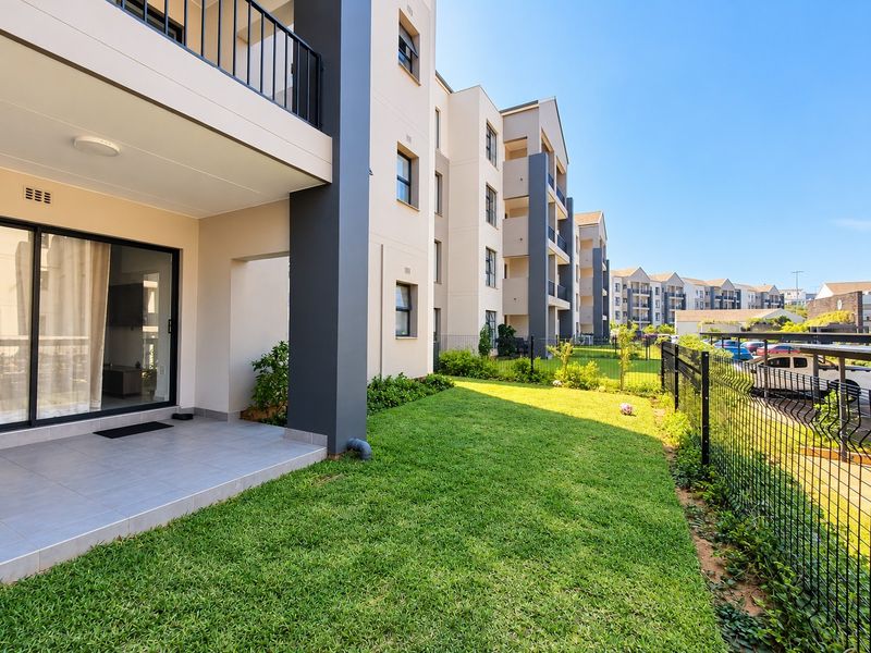 Ground floor apartment featuring a private tiled patio and a well-maintained garden area, enclosed by secure metal fencing.