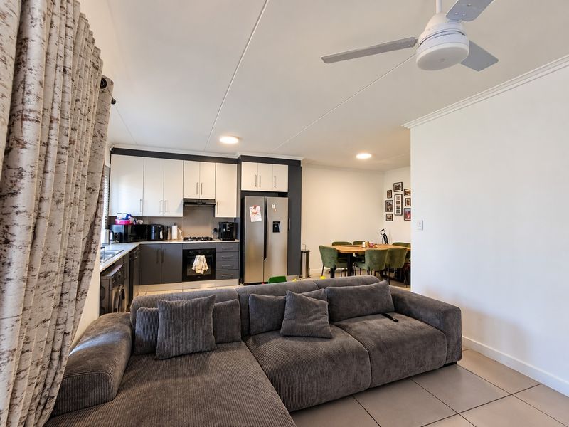An open-plan living and kitchen area featuring modern two-tone cabinetry, built-in appliances, tiled flooring, and a ceiling fan, creating a functional and cohesive living space.