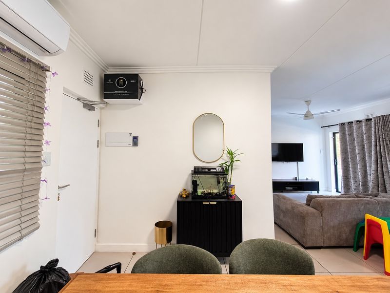 Open-plan living area featuring tiled flooring, a ceiling fan, and a wall-mounted energy storage system, seamlessly connecting to the adjacent lounge space.