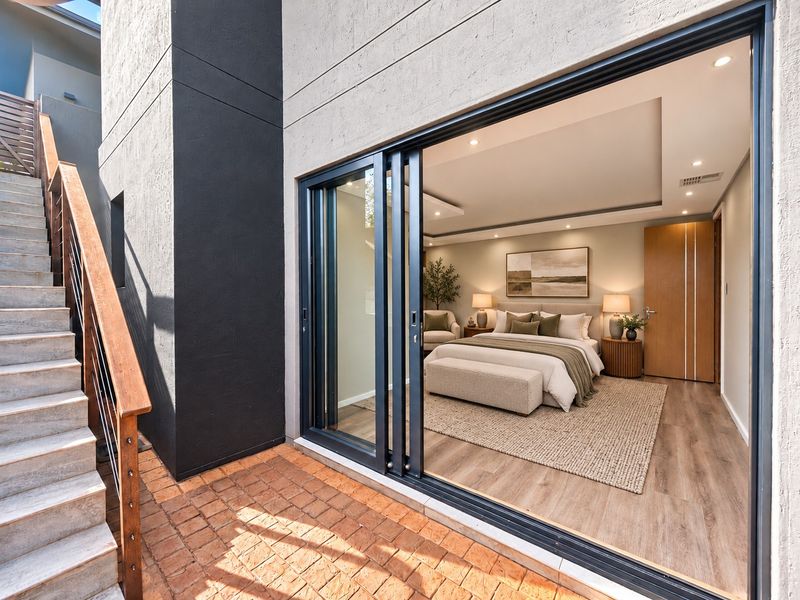 A modern bedroom featuring large sliding glass doors that open onto a private brick-paved patio with an adjacent timber staircase.