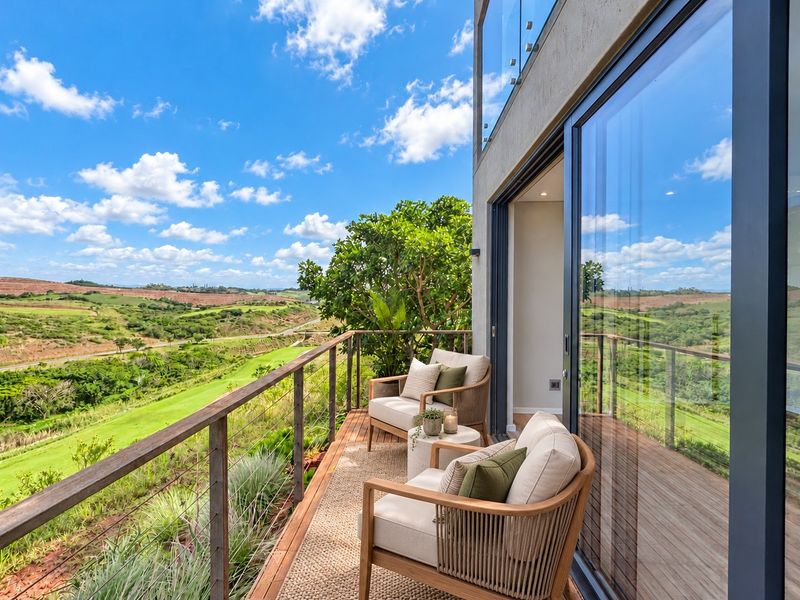 A modern balcony featuring timber decking and a glass balustrade, offering expansive views over the surrounding landscape.
