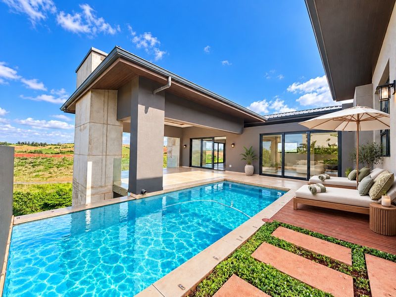 A modern outdoor pool area featuring a swimming pool, covered patio with sliding glass doors, timber decking, and scenic landscape views.