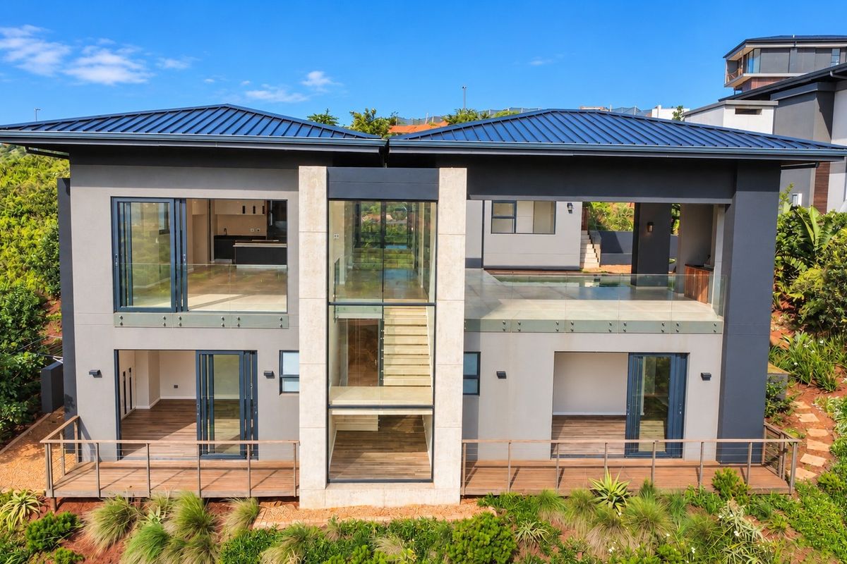 Aerial view of the modern rear facade featuring expansive glass sliding doors, timber decking, stone accents, and a swimming pool.