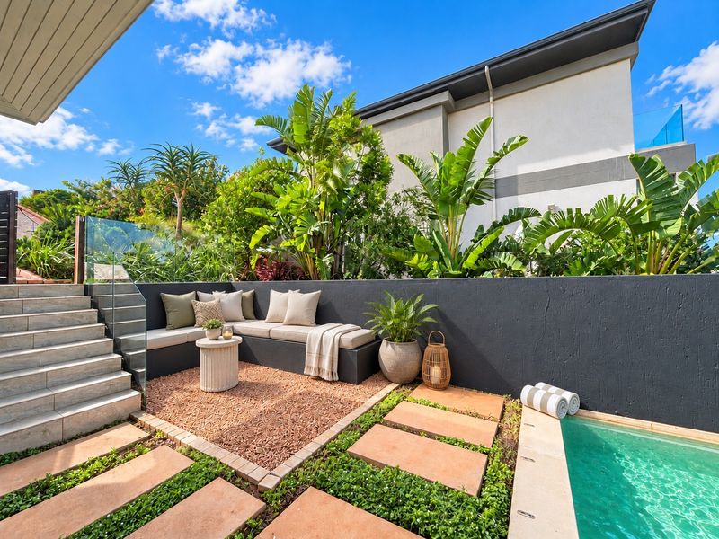 A beautifully landscaped pool area featuring a modern swimming pool, glass balustrade, tiled stairs, and a built-in bench seating area with a retaining wall.