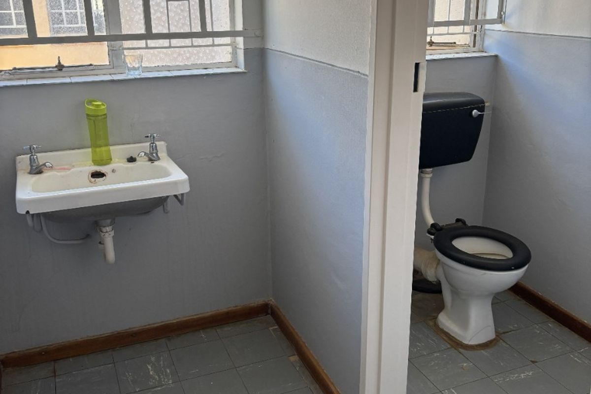 A functional bathroom featuring a wall-mounted basin and a separate toilet area with security bars on the windows and tiled flooring.